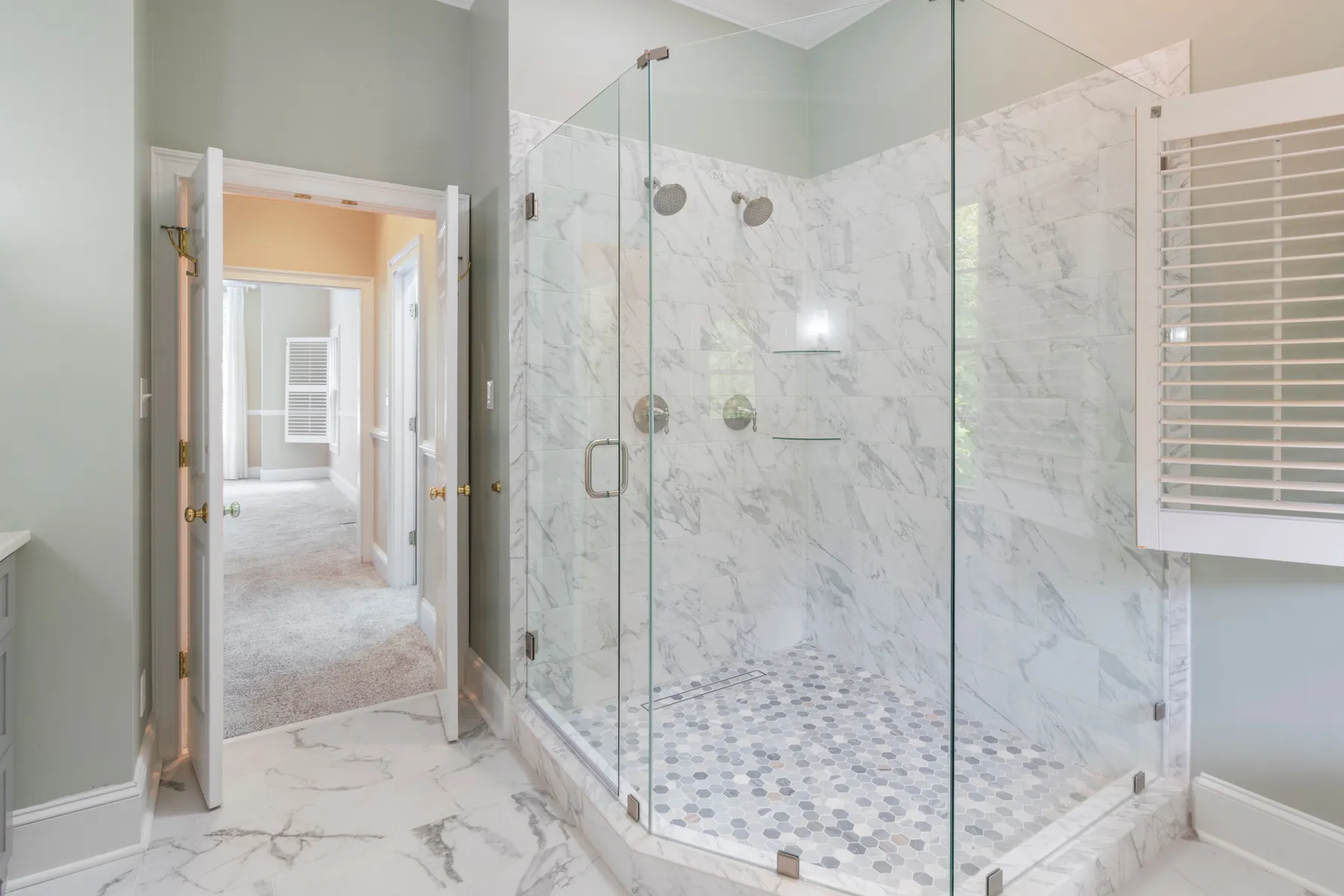 Marble-look tile walk-in shower with a frameless glass enclosure in a remodeled bathroom